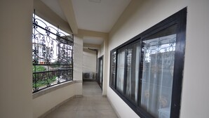 A corridor with a tiled floor, a window with decorative iron bars, and a view of a building outside. - Line-Residence (Douala)