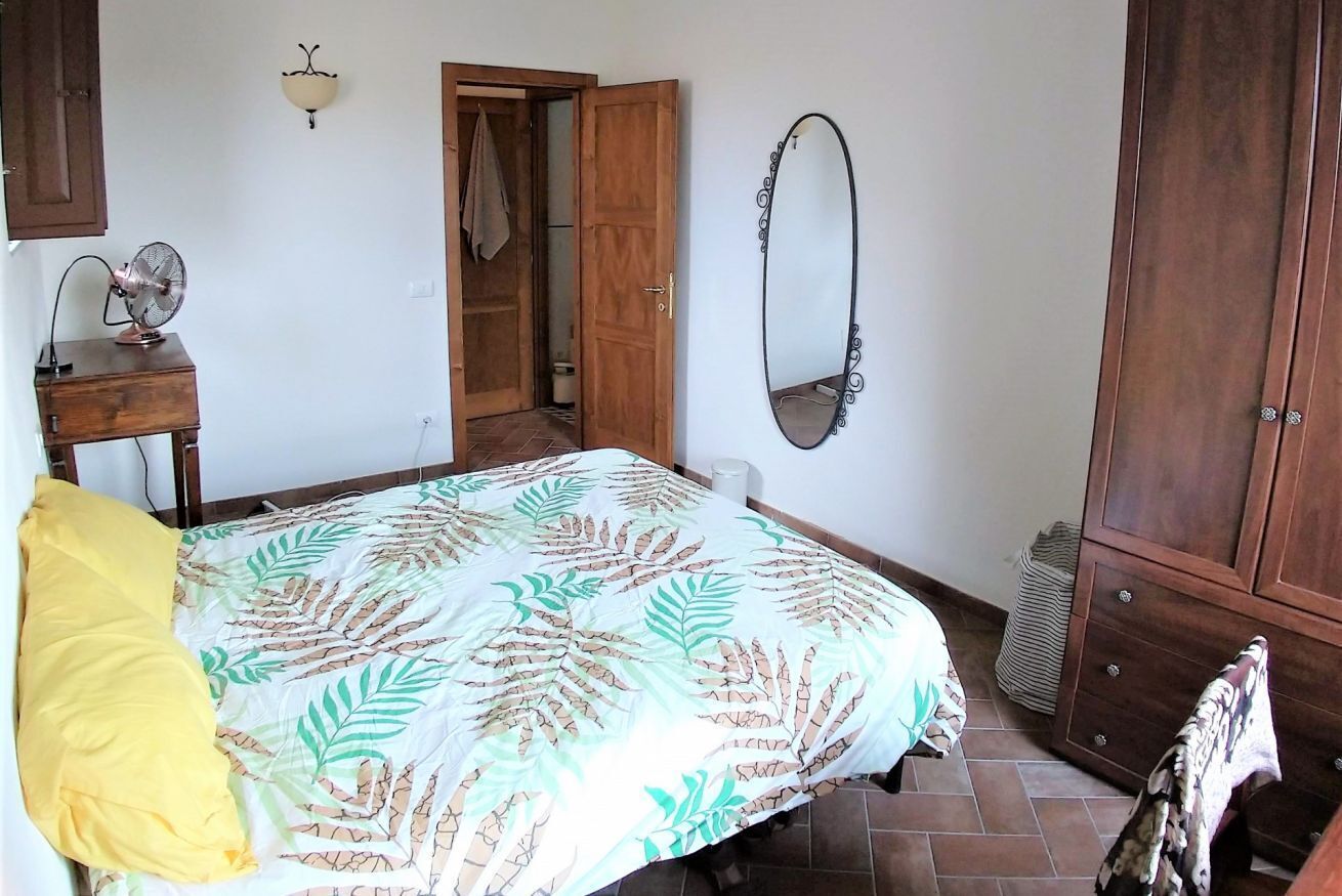 Un dormitorio con una cama, un armario de madera, un espejo y un ventilador sobre un tocador.