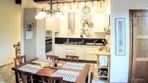 A dining area with a wooden table and chairs, a kitchen in the background with white cabinets, and a clock on the wall. - THE AERIE - THE EAGLE'S NEST - large apartment in strategic location (Siena)
