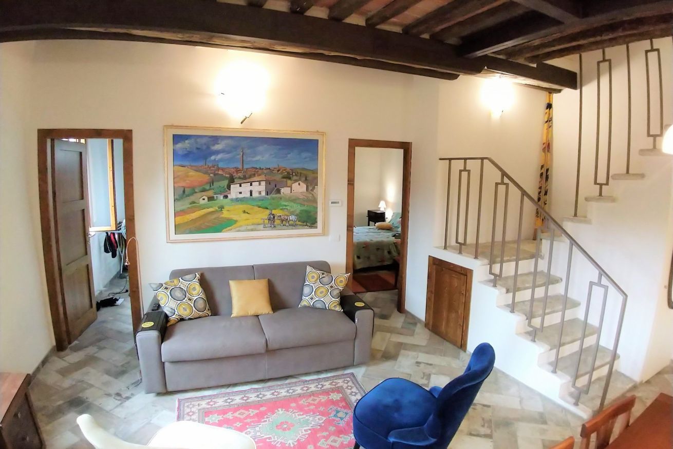 Un salon avec un canapé, un fauteuil bleu, un tableau au mur et un escalier.