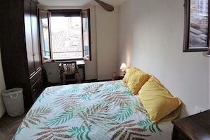 A bedroom with a bed, a window, a lamp, and a wooden wardrobe.