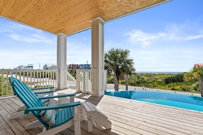 Um deck de madeira com piscina, duas cadeiras e vista para o oceano.
