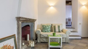 A living room with a fireplace, a sofa, a small table with a green tray, and a staircase leading upstairs. - Moma 1 (Como)
