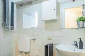 Une salle de bain équipée d’un WC, d’un lavabo, d’un miroir, d’un porte-serviettes et d’une plante en pot.
