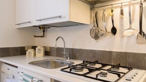 A kitchen with a gas stove, sink, and hanging utensils. - Moma 1 (Como)
