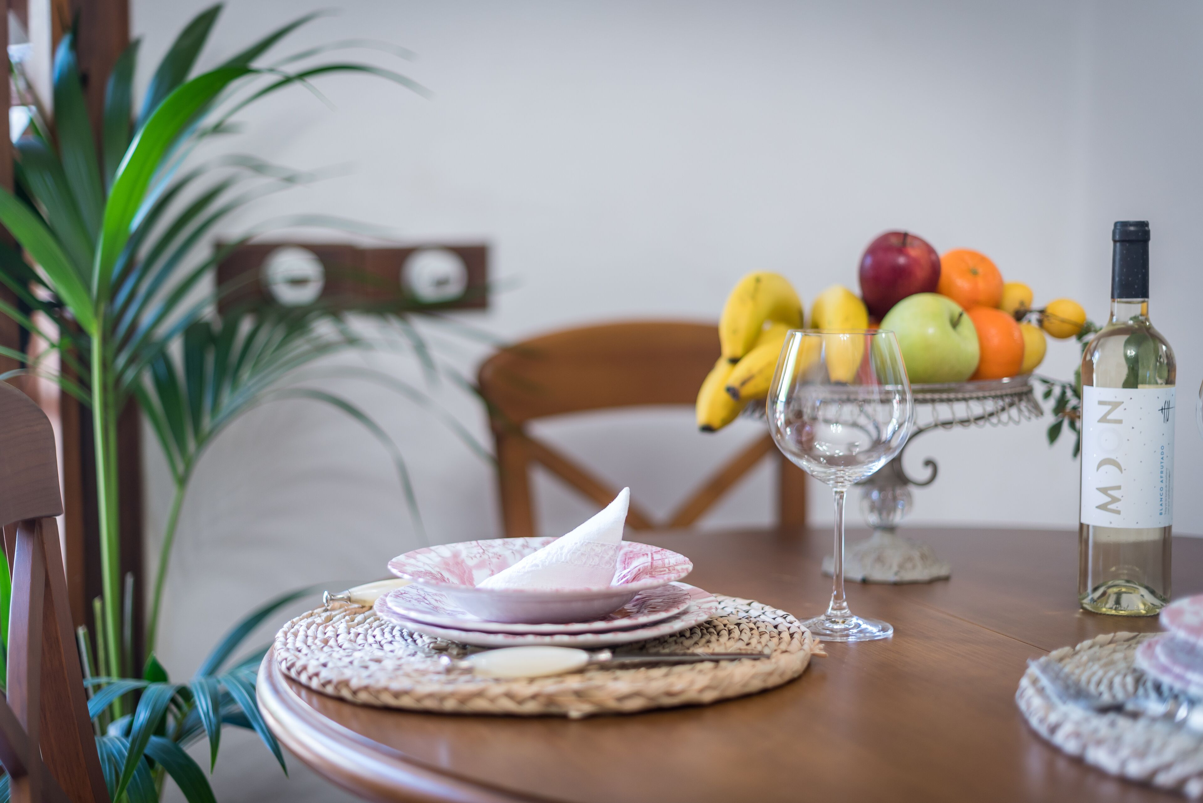 Een eettafel met een geweven placemat, een wijnglas en een fles wijn.