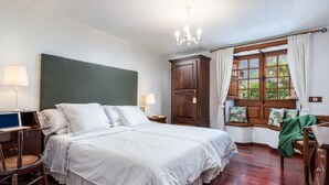 Camera da letto con un letto grande, una testata in legno, una scrivania con una sedia, una finestra con tende e un lampadario.
