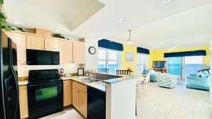 A modern kitchen with granite countertops, wooden cabinets, and black appliances. - Crystal Shores Condominiums by ALBVR (Gulf Shores)