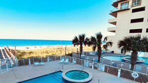 A pool area with a hot tub, lounge chairs, and a view of the beach. - Crystal Shores Condominiums by ALBVR (Gulf Shores)