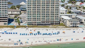 A beachfront hotel with multiple floors, a swimming pool, and beach umbrellas. - Crystal Shores Condominiums by ALBVR (Gulf Shores)