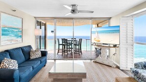 Un vaste espace de vie avec balcon, ventilateur de plafond, télévision et vue sur l’océan.