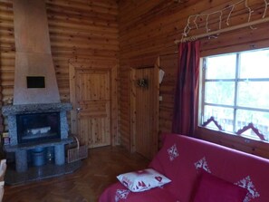 Interior acolhedor de uma cabana de madeira com lareira de pedra, porta de madeira e janela com cortinas.