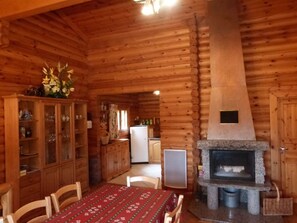 Ein Interieur einer Holzhütte mit Essbereich, einer Küche inklusive Kühlschrank und einem Kamin aus Stein.