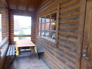Eine Blockhütte mit Holzinnenausbau, ein Fenster mit Blick auf ein Backsteingebäude und ein Picknicktisch mit Bänken.