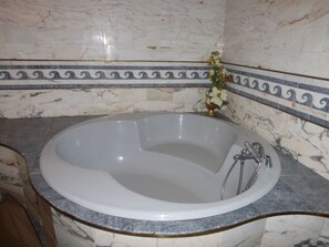 Um banheiro com banheira de mármore, um vaso dourado com flores e uma moldura decorativa.