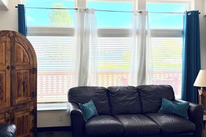 Ein Zimmer mit einer schwarzen Ledersofa, einem Holzschrank und einem Fenster mit weißen Vorhängen.