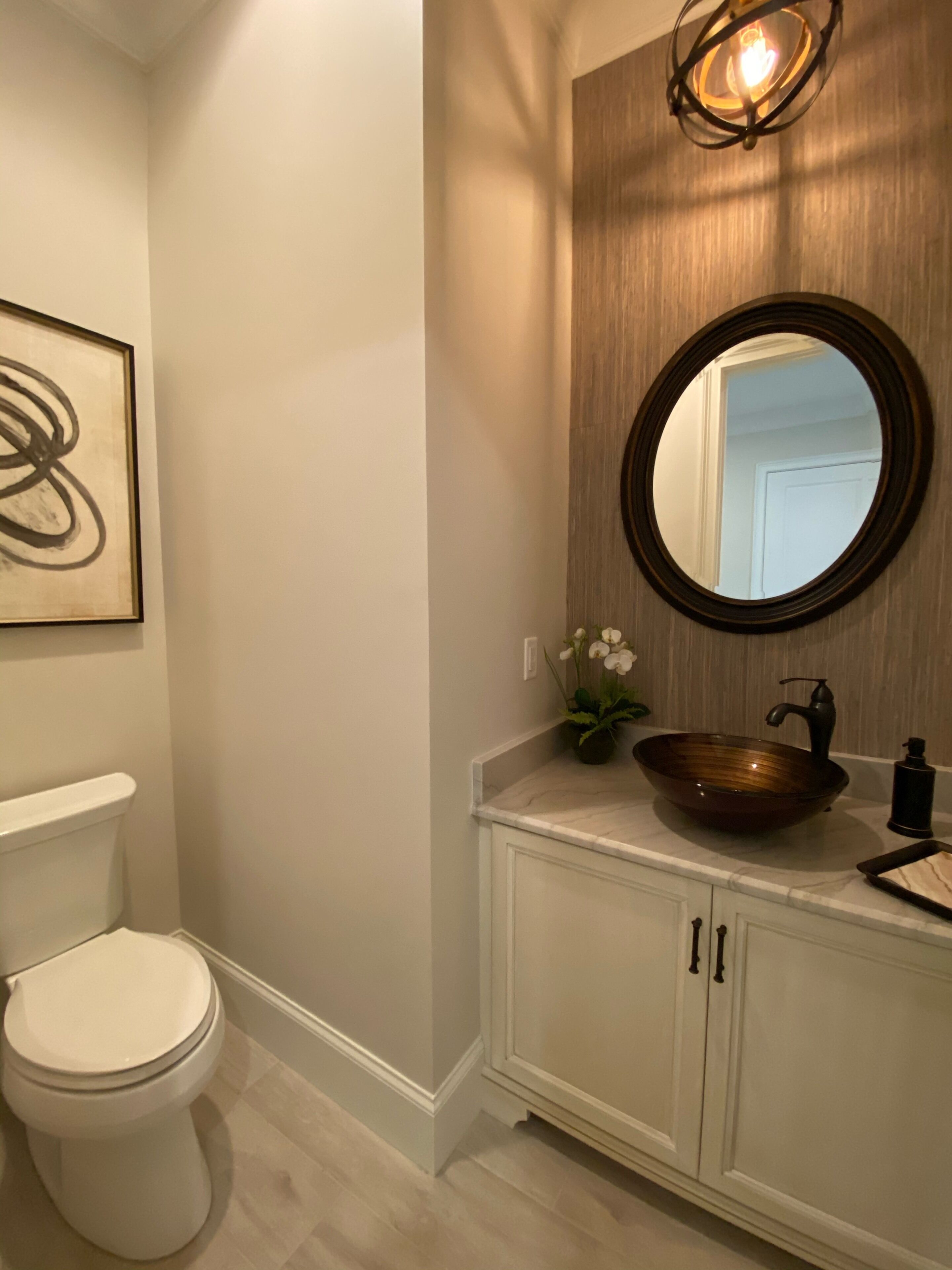 A bathroom with a white toilet, a wooden vanity with a vessel sink, a round mirror, and a wall-mounted light fixture.