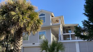 Une maison à deux étages avec un balcon, un garage et une pelouse bien entretenue agrémentée de palmiers.