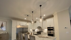 Une cuisine moderne avec des armoires blanches, des appareils en acier inoxydable et des luminaires suspendus.