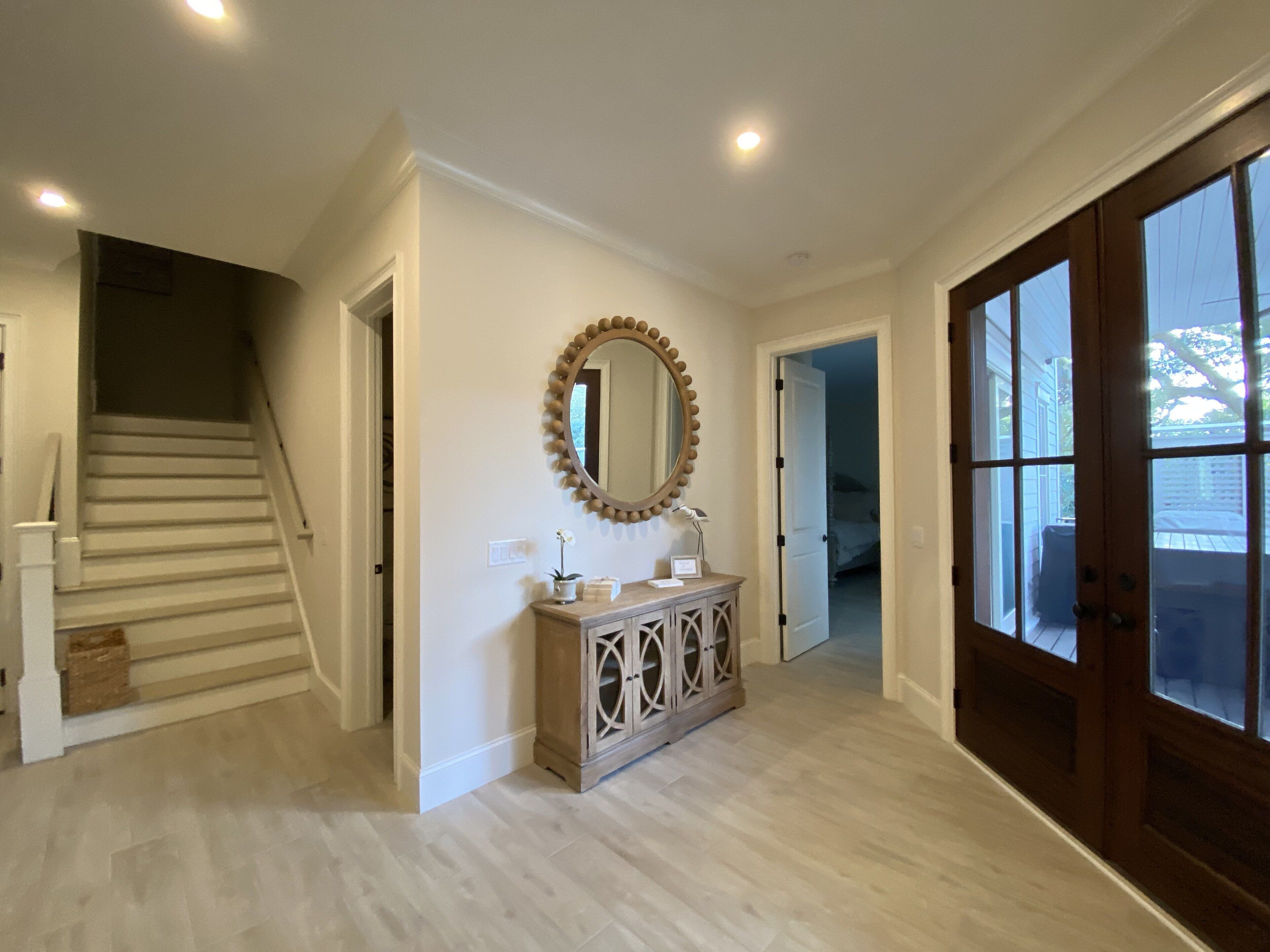 Un hall d’entrée spacieux avec un escalier en bois, un grand miroir et une console en bois.