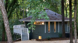 Une petite cabane aux couleurs sombres, dotée d’une terrasse en bois et d’un escalier menant à une fenêtre.