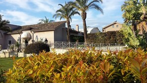 A building with a tiled roof, a white fence, and palm trees. - Hotel La Cavalera (Augusta)