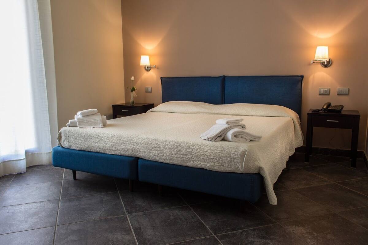 A neatly made bed with a blue headboard, two bedside tables with lamps, and a vase of flowers on one table.