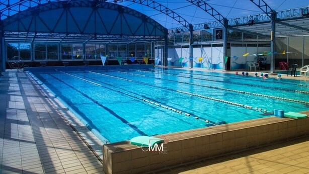 A large indoor swimming pool with multiple lanes, a covered spectator area, and a clear view of the sky. - Hotel La Cavalera (Augusta)