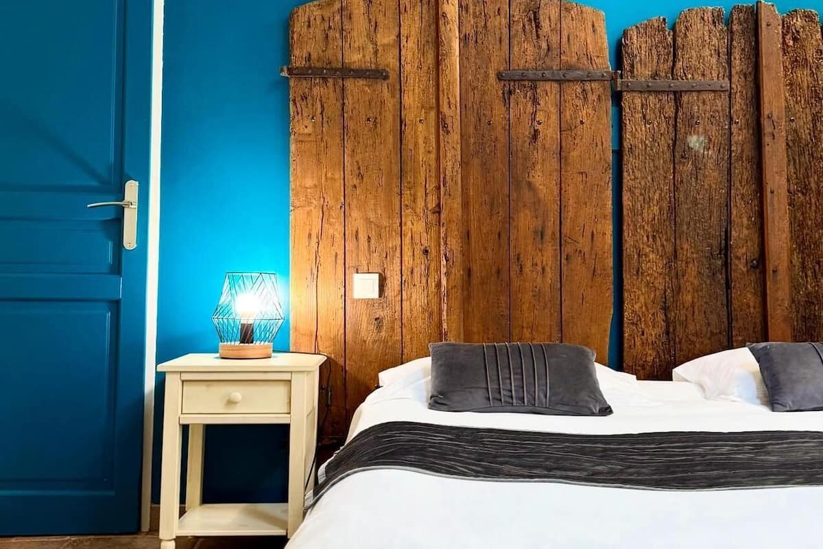 A bedroom with a bed, a nightstand, a lamp, and a wooden headboard.