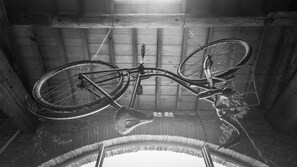 A bicycle hanging upside down in a wooden room with a brick wall and a window. - L'Alcove Hotel Restaurant (Villemur-sur-Tarn)