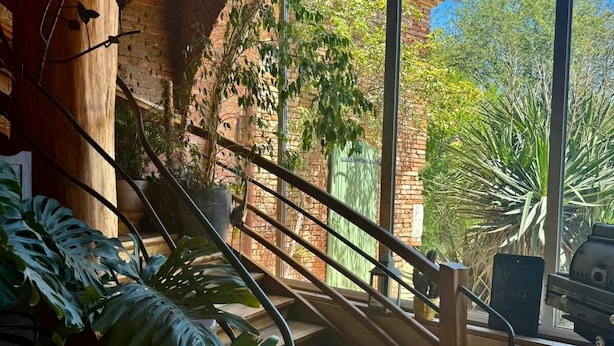 Una escalera con barandilla metálica que lleva a un balcón con vistas a la vegetación y un edificio de ladrillo.