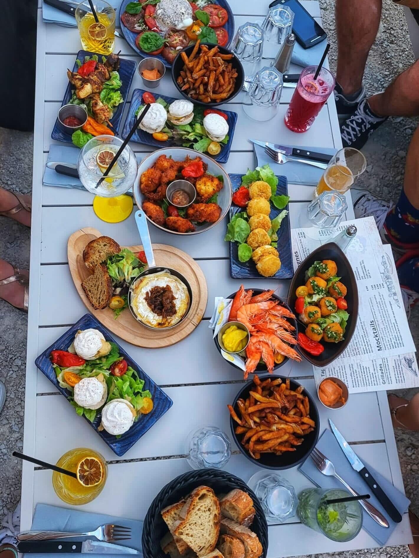 Une table dressée avec divers plats, notamment des fruits de mer, des salades et du pain, ce qui laisse supposer qu’un repas va être servi.
