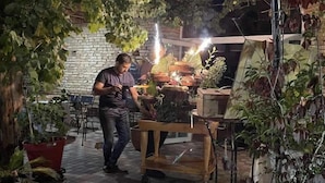 Una persona de pie cerca de un carrito con plantas y una mesa con diversos objetos.