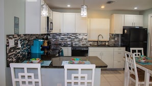 A modern kitchen with white cabinets, a black refrigerator, and a dining area with white chairs and a wooden table.