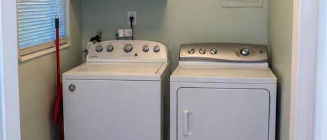 A laundry room with two white washing machines, a red mop, and a trash can.
