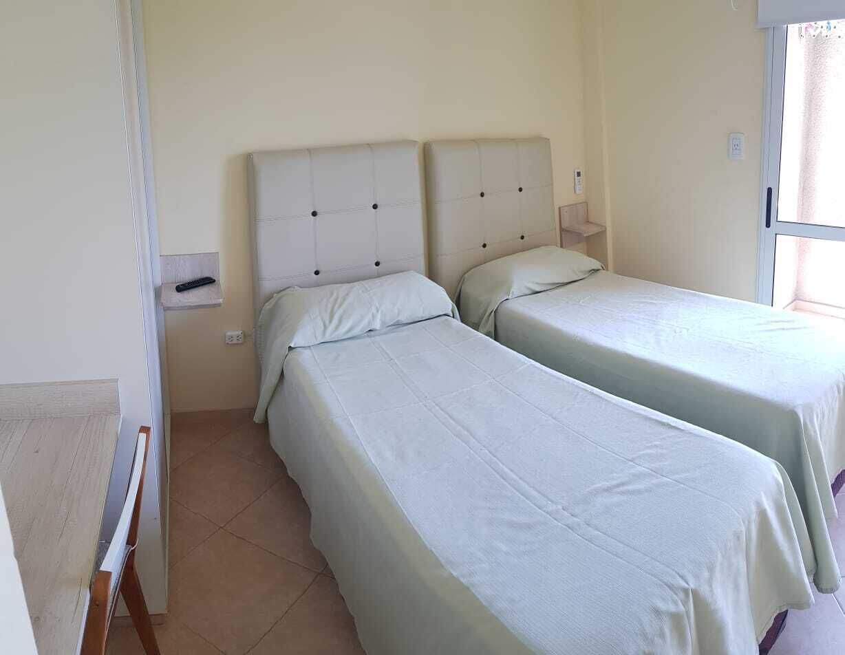 Una habitación de hotel con dos camas individuales, una mesita de noche pequeña y un ventanal con cortinas.
