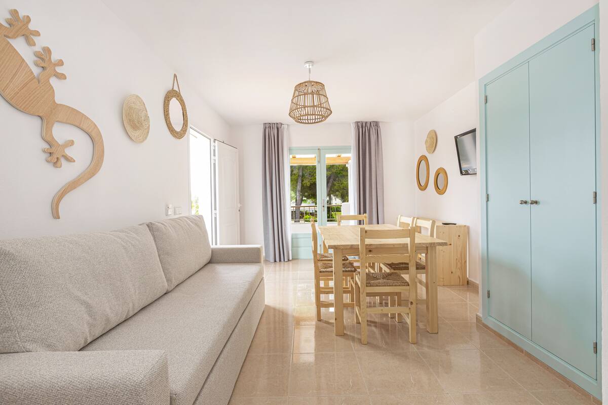 A modern living room with a sofa, dining table, chairs, and a TV on a wall.