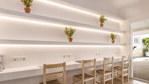 Een moderne kamer met een wit bureau, vier houten stoelen en planken met potplanten.