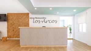 Een receptiegedeelte met een houten wand, een grijze receptiebalie en een bordje met de tekst 'apartamentos los Arcos'.