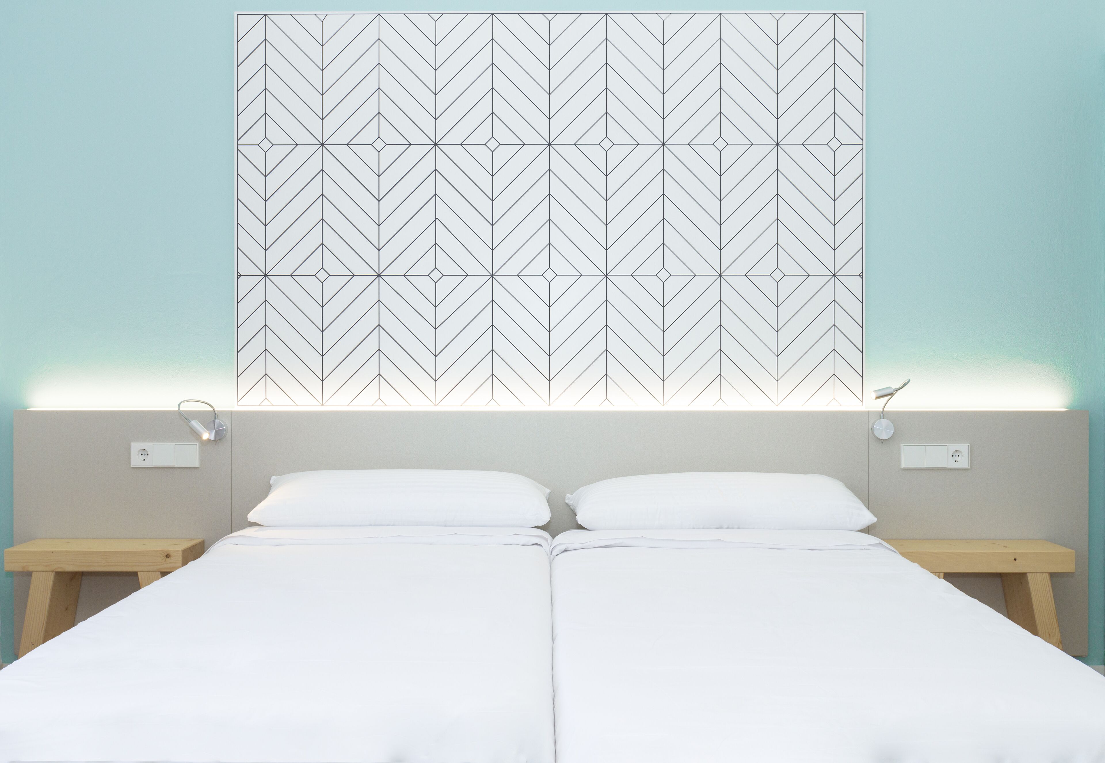 Ein Doppelbett mit weißen Leinen, zwei Nachttische und ein Wandbehang mit geometrischem Muster.