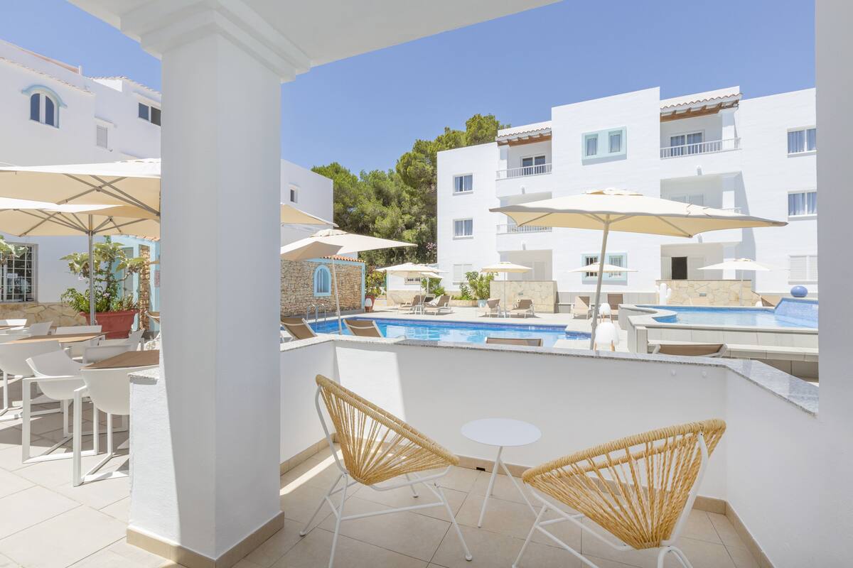 A poolside area with white walls, wicker chairs, and umbrellas.
