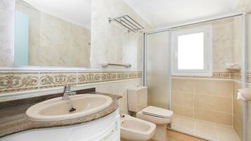 Un baño con lavamanos, inodoro, bidé y cabina de ducha de vidrio.