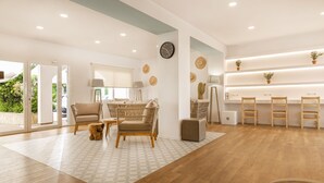 Een modern interieur met een houten vloer, een eethoek met rieten meubels en een receptiebalie met planten.