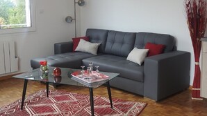 A modern living room with a grey sofa, red cushions, a glass coffee table, and a red patterned rug.