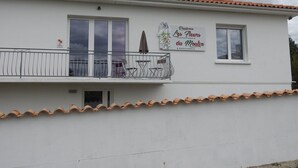 A building with a balcony, a sign advertising 'Residence Les Fleurs du Moulin', and a terrace with chairs and a table.