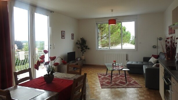 A spacious living room with a dining area, a sofa, a coffee table, and a large window providing a view of the outdoors.