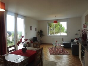 Uma sala de estar espaçosa com área de jantar, sofá, mesa de centro e uma grande janela com vista para o exterior.