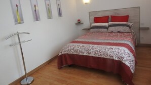 A bedroom with a bed, a bedside table, a wall-mounted shelf with a vase, and a floor lamp.