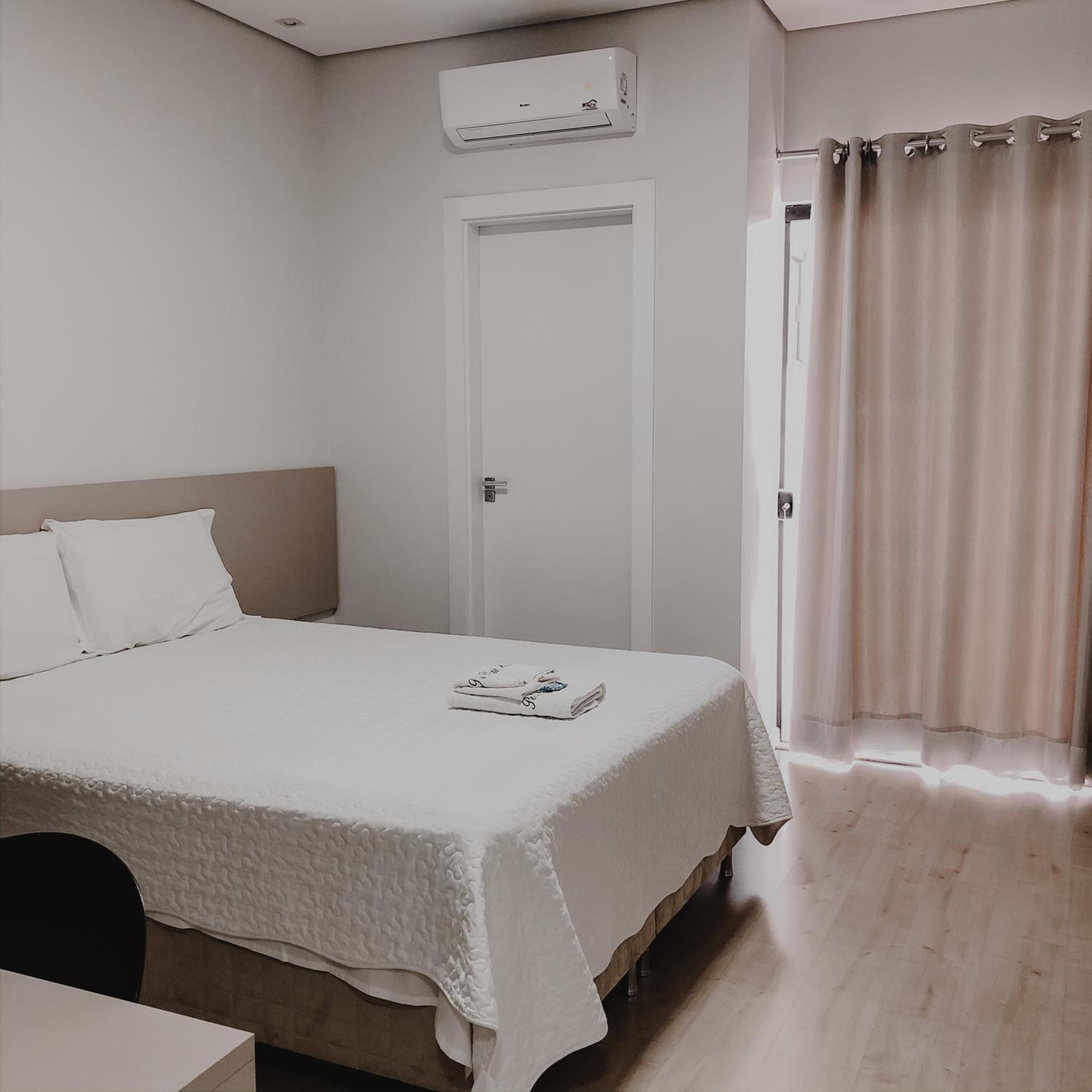 A bedroom with a bed, a door, an air conditioning unit, and a window with curtains.