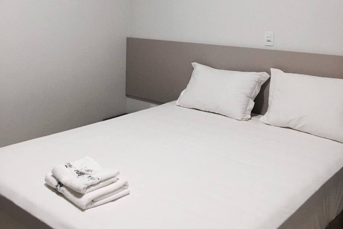 Habitación de hotel con cama, dos almohadas, una toalla doblada y un aire acondicionado de pared.